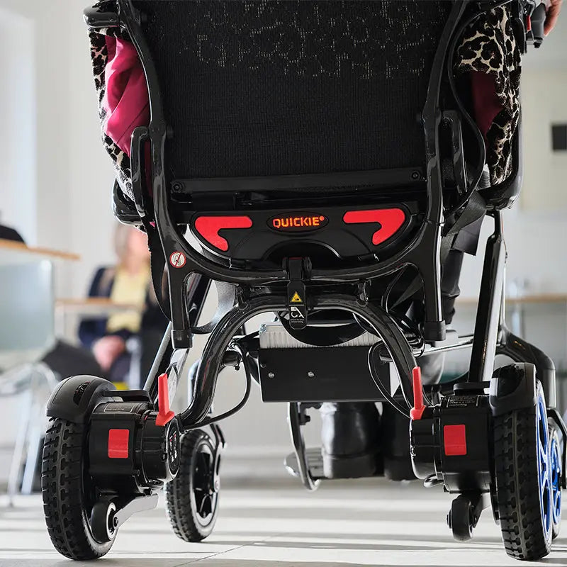Close-up of a Mobility World Ltd UK - Quickie Q50 R Carbon Folding Powerchair , showing the wheels and seat structure.