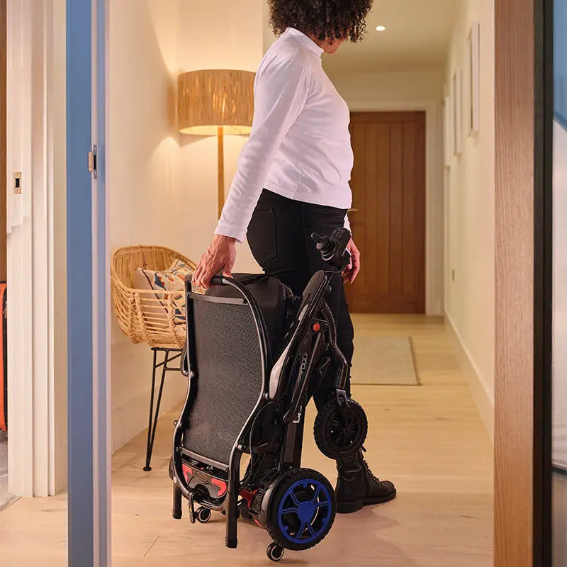 Person pushing a folded Quickie Q50 R Carbon Folding Powerchair through a doorway.