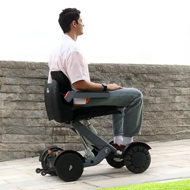 Person using a Mobility World Ltd UK: XSTO M4 Electric Powered Wheelchair outdoors near a stone wall.