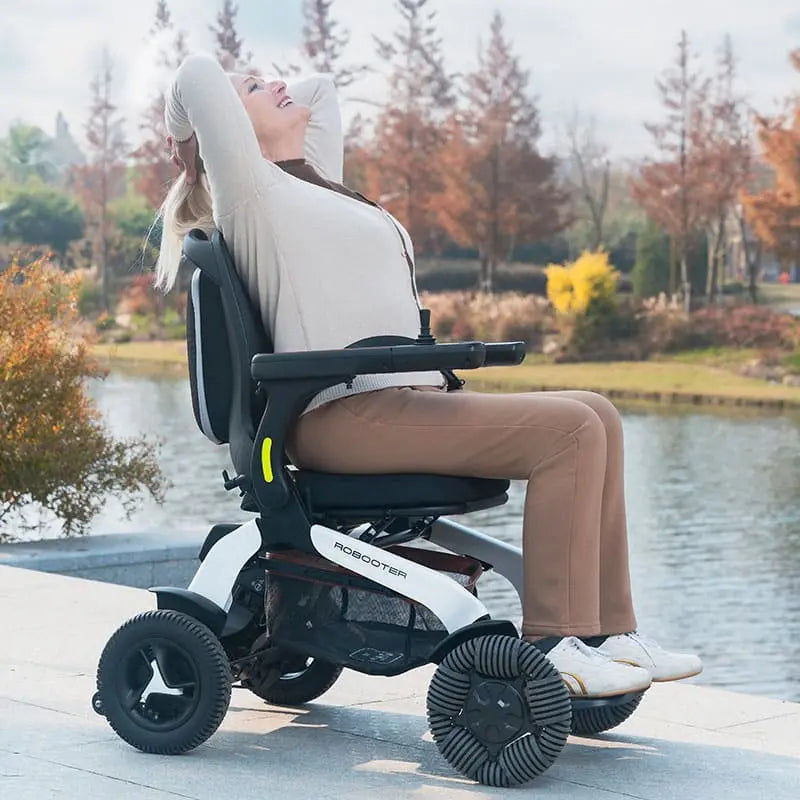 Person using Robooter E60 Pro All Terrain Electric Folding Powerchair by a lake with trees in the background
