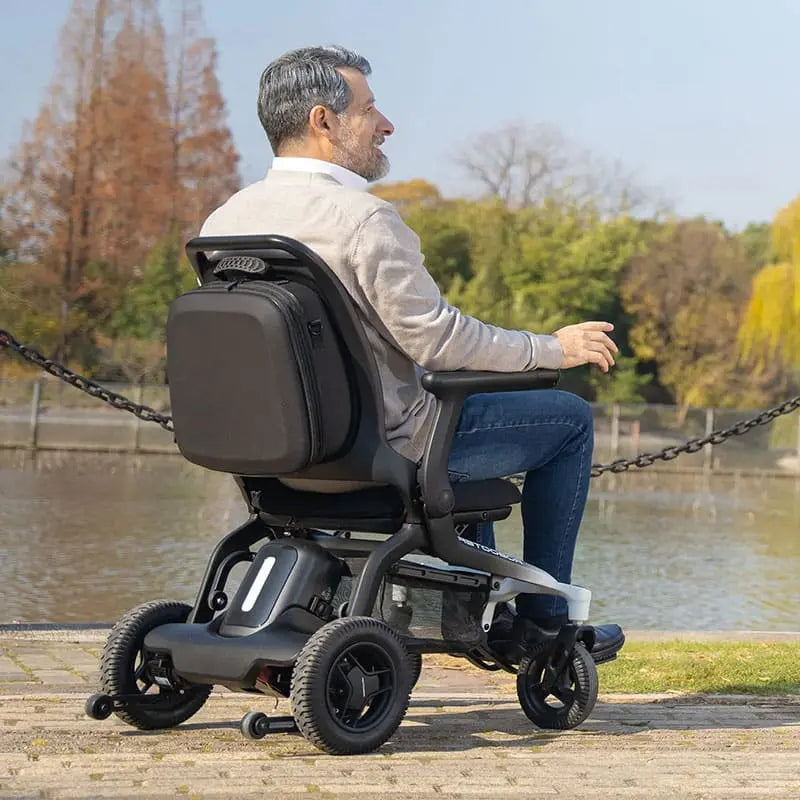 Man using a Robooter E80 Ultra Carbon Fiber Lightweight Folding Powerchair by a lake with trees in the background