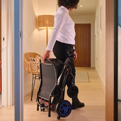 Person pushing a folded Quickie Q50 R Carbon Folding Powerchair  through a doorway.
