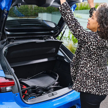 Woman in leopard print coat opening a blue car trunk with a folded Quickie Q50 R Carbon Folding Powerchair  inside.