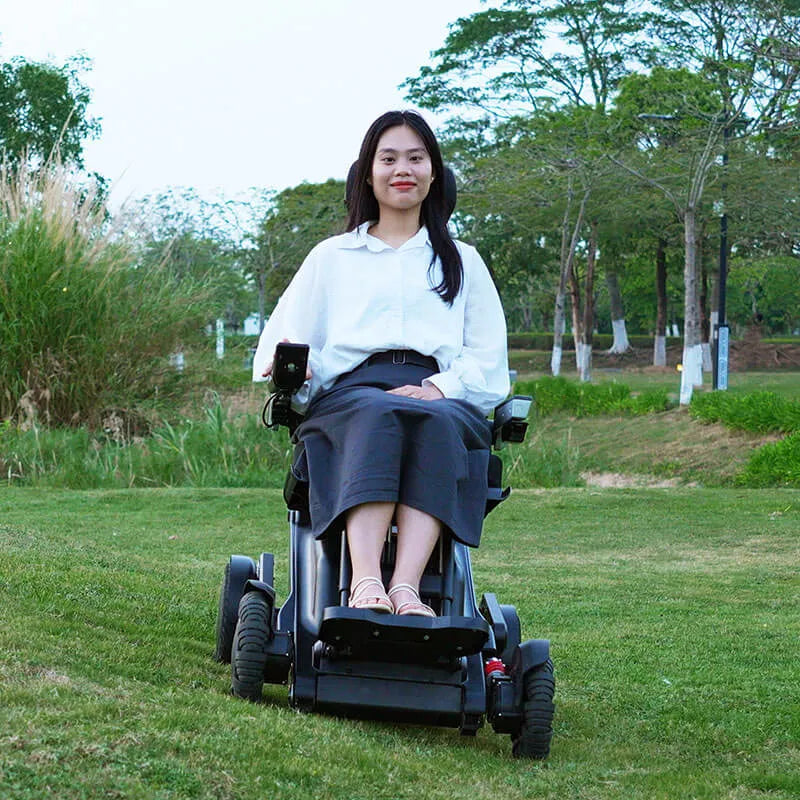 Woman in a Xsto X12 All-Terrain Mobility Robot Powered Wheelchair
 sitting on grass with trees in the background