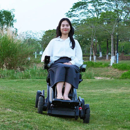 Woman in a Xsto X12 All-Terrain Mobility Robot Powered Wheelchair
 sitting on grass with trees in the background