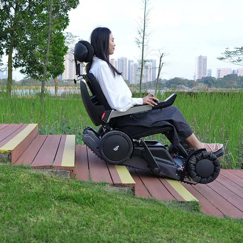 Person using a Xsto X12 All-Terrain Mobility Robot Powered Wheelchair
 in an outdoor setting with greenery and buildings in the background