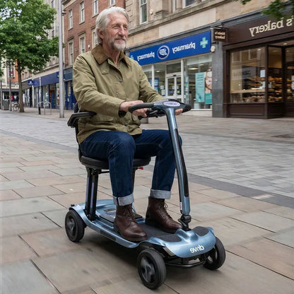 Man riding AeroMg Lightweight Folding Mobility Scooter on a city street with shops in the background
