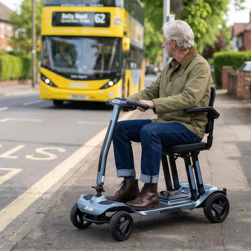Man riding a AeroMg Lightweight Folding Mobility Scooter on a street with a yellow bus in the background