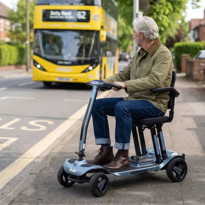 Man riding a AeroMg Lightweight Folding Mobility Scooter on a street with a yellow bus in the background