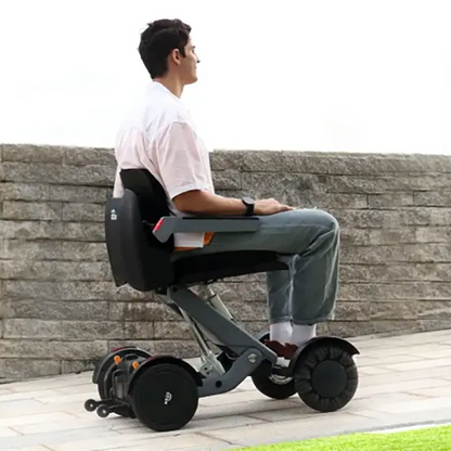 Person using a Mobility World Ltd UK: XSTO M4 Electric Powered Wheelchair outdoors near a stone wall.