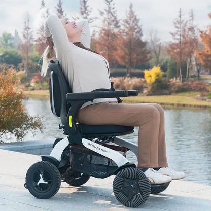 Person using Robooter E60 Pro All Terrain Electric Folding Powerchair by a lake with trees in the background