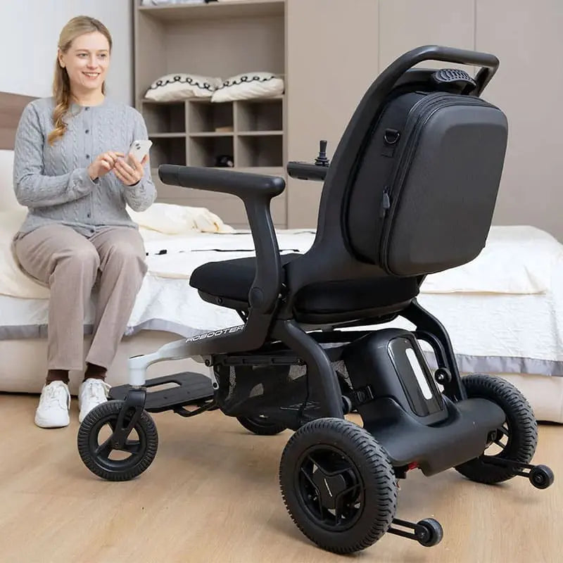 Person using a smartphone next to a Robooter E80 Ultra Carbon Fiber Lightweight Folding Powerchair in a room.