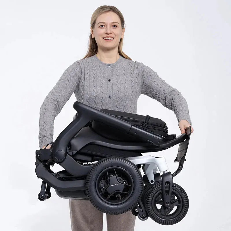 Woman holding a folded Robooter E80 Ultra Carbon Fiber Lightweight Folding Powerchair